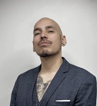 a bald man in a suit with tattoos on his chest