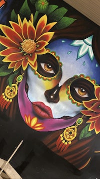 a painting of a day of the dead woman with flowers on her face