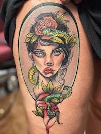 a tattoo of a woman with a snake on her thigh