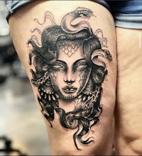 a tattoo of a woman with snakes on her thigh