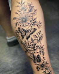 a black and white tattoo of flowers and butterflies on a woman's leg