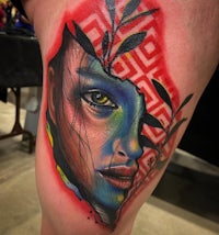 a tattoo of a woman with a colorful face on her thigh