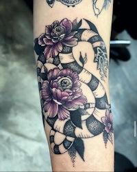 a tattoo of a snake and flowers on the forearm