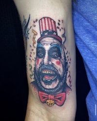 a tattoo of a clown with a hat on his arm